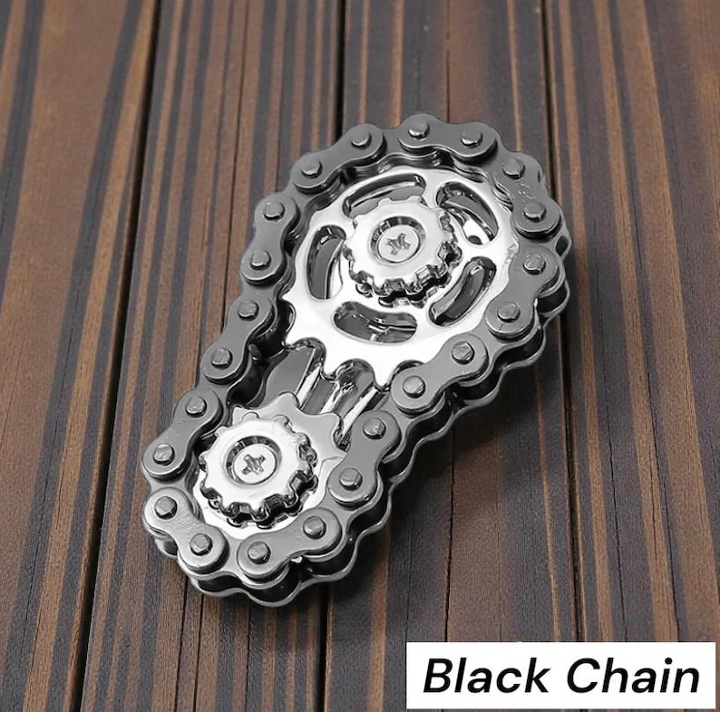May include: A silver and black metal chain design with gears and the text "Black Chain" on a wooden surface. The chain is arranged in an oval shape, with two gears in the center.