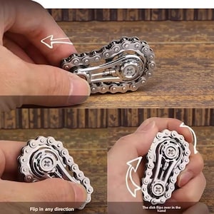 May include: A silver-colored fidget toy resembling a bicycle chain. The toy has a central disk with a cross-shaped design and is held in a person's hand. The text "Flip in any direction" and "The disk flips over in the hand" are visible.