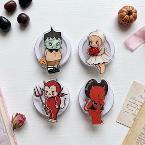 May include: Four acrylic pins featuring vintage-style illustrations of Halloween characters: a green Frankenstein monster, a white ghost, a red devil with a pitchfork, and a red devil with horns. Each pin is mounted on a circular white base.