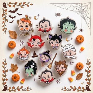 May include: A collection of twelve acrylic charms featuring illustrated baby characters dressed in Halloween costumes, including a pumpkin, vampire, Frankenstein, devil, cat, mummy, clown, witch, bride of Frankenstein, and werewolf, with scattered candy corn and pumpkins.