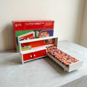 Può includere: Un set da camera per bambole vintage con un comò bianco e rosso, un letto con un materasso a fantasia floreale e una scatola con testo in italiano. Il set include un piccolo comodino con due ante rosse.