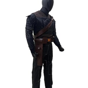 May include: A black costume with white stitching, featuring a high-collared top, shoulder armor, and a brown leather belt with a holster. The costume includes black pants and a brown shoulder strap.