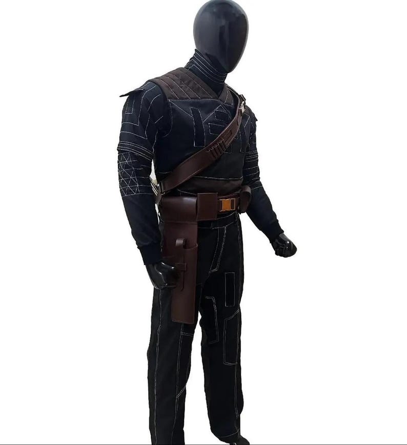 May include: A black costume with white stitching, featuring a high-collared top, shoulder armor, and a brown leather belt with a holster. The costume includes black pants and a brown shoulder strap.