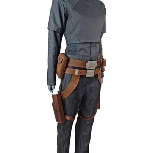 May include: A gray costume with a high collar, short-sleeved top, and long sleeves. The costume includes dark gray pants, a brown leather belt with a silver buckle, and brown leather holsters. The outfit is displayed on a mannequin.