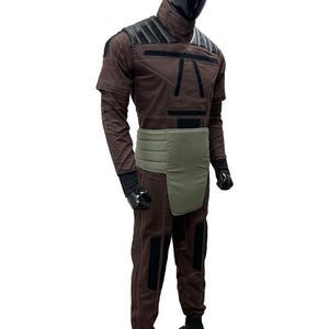 May include: A brown jumpsuit with black detailing and a green waist wrap is displayed on a mannequin. The outfit features short sleeves, a high collar, and black gloves. The mannequin has a black head and is standing on a black base.