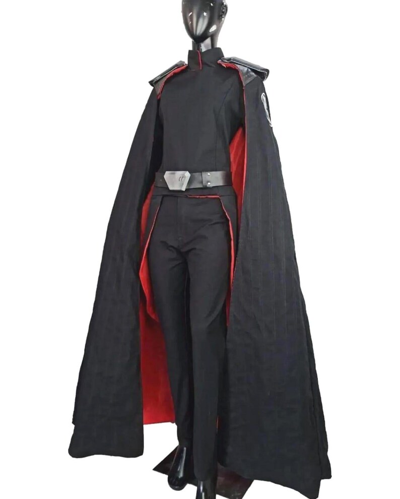 May include: A black costume with a red-lined cape, featuring a high-collared jacket, matching pants, and a belt. The costume includes shoulder accents and a small emblem on the sleeve, displayed on a mannequin.