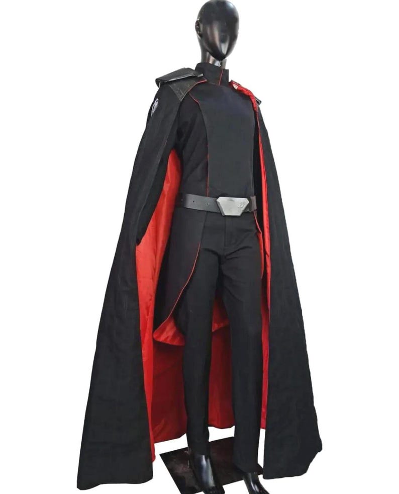 May include: A black costume with a red-lined cape, displayed on a mannequin. The outfit includes a black top, pants, and belt with a silver buckle. The cape has a high collar and shoulder accents.