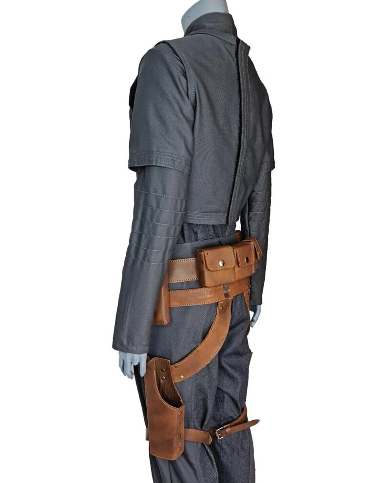 May include: A gray jacket and pants ensemble with a brown leather belt and holster. The jacket has a high collar and a zipper down the back. The belt features multiple pouches and a leg strap.