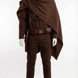 May include: A brown costume displayed on a mannequin. The outfit includes a long-sleeved shirt, pants, belt with pouches, a holster, and a draped shawl. The boots are brown leather.
