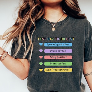 May include: Dark gray t-shirt with the text "TEST DAY TO-DO LIST" and colorful bullet points: Spread good vibes, Drink coffee, Stay positive, More coffee, and Say "You got this!".