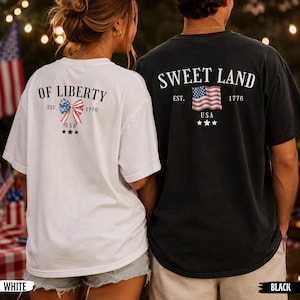K&ouml;nnte beinhalten: Ein wei&szlig;es T-Shirt mit dem Text OF LIBERTY EST. 1776 USA und einer patriotischen Schleifengrafik sowie ein schwarzes T-Shirt mit dem Text SWEET LAND EST. 1776 USA und einer US-Flaggen-Grafik, beide mit drei kleinen Sternen unter den Motiven.