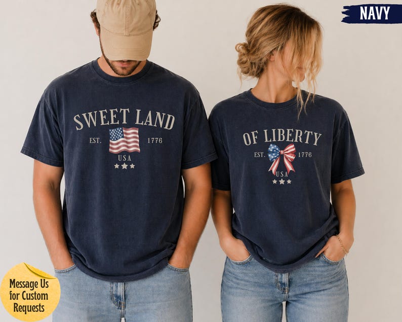 K&ouml;nnte beinhalten: Zwei marineblaue T-Shirts mit wei&szlig;em Text und patriotischen Grafiken. Das linke T-Shirt zeigt SWEET LAND mit einer USA-Flagge, EST. 1776 und drei Sternen. Das rechte T-Shirt zeigt OF LIBERTY mit einer Schleife im USA-Flaggen-Design.