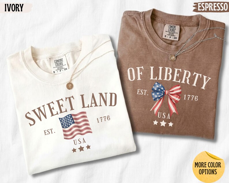 K&ouml;nnte beinhalten: Zwei kurz&auml;rmelige T-Shirts mit Rundhalsausschnitt in Elfenbein und Espresso. Das elfenbeinfarbene Shirt zeigt den Text SWEET LAND, eine US-Flagge, EST. 1776 und drei Sterne. Das Espresso-Shirt zeigt den Text OF LIBERTY, eine Schleife, EST. 1776 und drei Sterne.