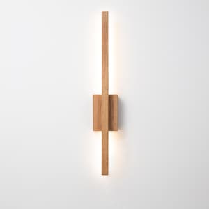 May include: A modern, minimalist wall sconce made of light-colored wood. The design features a vertical rectangular light element intersected by a square block, with a warm, diffused glow emanating from the light source. This fixture is ideal for contemporary home decor.