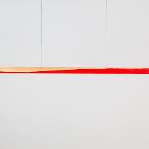 Puede incluir: Lámpara colgante lineal moderna. Presenta una sección de madera natural con un acento rojo vibrante. La lámpara está suspendida por dos cables finos sobre un fondo blanco. El diseño es minimalista y contemporáneo. Mide unos 100 cm de largo.