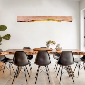 Könnte beinhalten: Ein modernes Esszimmer mit einem großen Holztisch und sechs schwarzen Stühlen. Über dem Tisch hängt eine lange, rechteckige Holzleuchte. Eine große Pflanze und ein Weidenkorb befinden sich in der Ecke. Der Raum hat ein minimalistisches Design.