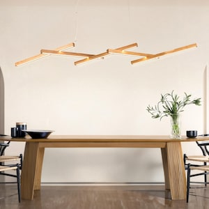 Può includere: Un moderno allestimento per la sala da pranzo con un tavolo in legno chiaro e sedie nere con sedute intrecciate. Un'esclusiva lampada in legno è appesa sopra il tavolo. Oggetti decorativi e un vaso di verde completano la scena.