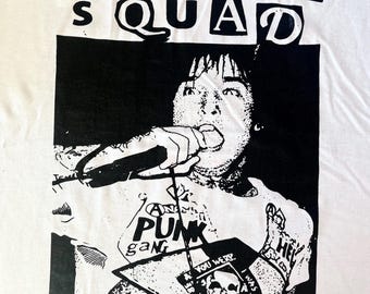 May include: White t-shirt with a black and white graphic of a person singing into a microphone. The shirt features the text "MONSTER SQUAD" and other punk-related graphics, including a skull and the words "PUNK gang".