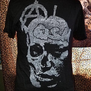 May include: Black t-shirt featuring a white skull graphic. The skull is made up of small white dots and has a crown on top. The crown is also made of small white dots.