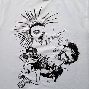 以下が含まれることがあります： 白いTシャツに、モホークのついたパンクロックな頭蓋骨2つの白黒のグラフィックプリント。頭蓋骨は服を着てアクセサリーをつけています。1つの頭蓋骨はマイクを持っています。