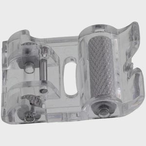May include: A clear plastic sewing machine attachment with a textured roller and various mechanical components. The attachment is designed to guide fabric during sewing. The design includes a roller and several clear plastic parts.