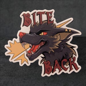 May include: A sticker featuring a stylized black wolf with red eyes and an open mouth, baring its teeth. The sticker has the words "BITE BACK" in a stylized font. A yellow burst emanates from the wolf's mouth.