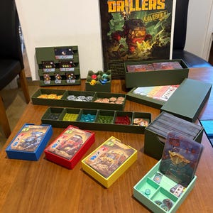 May include: A board game set titled Drillers including a rulebook, various coloured plastic card holders in blue, red, yellow, and light green, a multi-compartment olive green tray with small coloured tokens, and stacks of illustrated game cards.