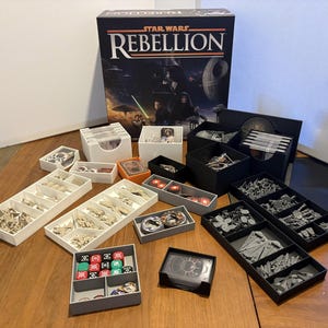 Pode incluir: Um jogo de tabuleiro Star Wars Rebellion com vários organizadores de plástico branco, preto e cinza contendo naves espaciais em miniatura, cartas de jogo e dados multicoloridos com símbolos. A caixa mostra Darth Vader e a Estrela da Morte.