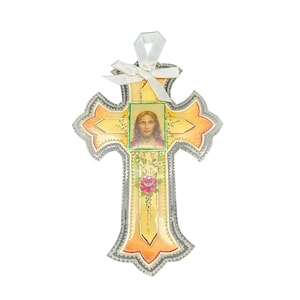 May include: A decorative cross with a picture of Jesus Christ. The cross is yellow and orange with a silver trim. A white ribbon is attached to the top. A pink rose is at the bottom.
