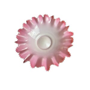 May include: A pink and white glass bowl with a ruffled edge. The bowl has a circular shape with a central, raised area. The rim of the bowl is a darker shade of pink.