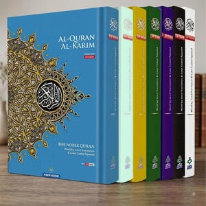 Pode incluir: Uma coleção de seis livros de capa dura intitulados Al-Quran Al-Karim, The Noble Quran, apresentando um grande volume azul com padrões dourados estilo mandala e cinco lombadas mais finas em verde claro, amarelo, verde escuro, roxo, preto e branco.