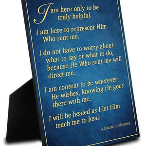 May include: A framed blue plaque with gold text. The text reads, "I am here only to be truly helpful." Additional text includes, "A Course in Miracles." The plaque is propped up by a black stand.