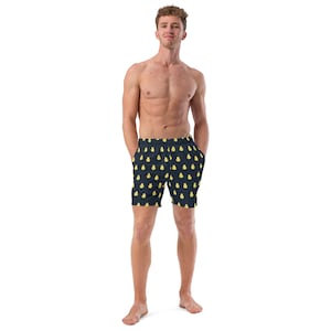 May include: Navy blue swim trunks with a repeating pattern of yellow pear shapes. The trunks have a drawstring waist and pockets. The model is standing and wearing the trunks.