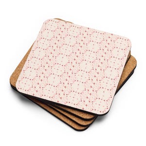 Puede incluir: Una pila de posavasos cuadrados con base de corcho y parte superior estampada. La parte superior presenta un diseño repetido de pequeños corazones rosas sobre un fondo crema. Los posavasos están apilados.