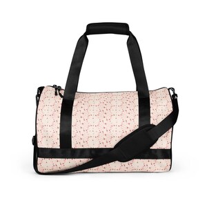 Puede incluir: Bolsa de lona crema con un patrón de estrellas rojas repetidas. La bolsa tiene asas negras, una correa para el hombro y una banda negra en la parte inferior. La bolsa está diseñada para transportar artículos.