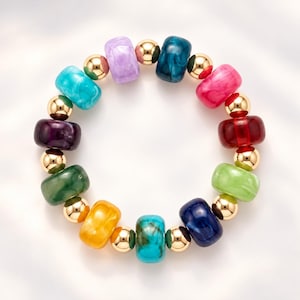 May include: A circular bracelet featuring alternating smooth gold-tone spherical beads and larger, cylindrical beads in a variety of marbled colors including purple, teal, pink, red, lime green, dark blue, turquoise, yellow, dark green, and deep purple.