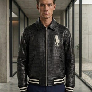 Könnte beinhalten: Eine schwarze Lederjacke mit Krokodilprägung, ausgestattet mit einem durchgehenden Frontreißverschluss, einem klassischen Kragen sowie gerippten Bündchen und Saum mit weißen Streifen. Auf der linken Brust befindet sich ein weißes Logo.