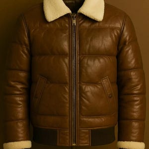 Può includere: Un giubbotto imbottito in pelle marrone con colletto in ecopelliccia color crema, chiusura centrale con zip in metallo, due tasche laterali con bottoni a pressione e polsini in maglia a coste marrone scuro sulle maniche e sul fondo.