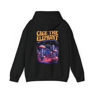 May include: Black hoodie featuring the text "CAGE THE ELEPHANT" in orange above a colorful desert landscape graphic. The graphic includes stylized mushrooms, cacti, and a starry night sky. The hoodie has a hood and long sleeves.