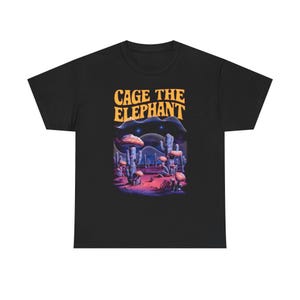 May include: Black t-shirt featuring a desert landscape design with mushrooms and cacti. The text "CAGE THE ELEPHANT" is printed in orange above the landscape. The design includes a night sky with stars.