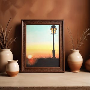 May include: A framed watercolor painting of a sunset with a lamppost silhouette. The painting is in a dark brown, ornate frame. Two-tone vases with dried plants are in the foreground, creating a warm, inviting scene.