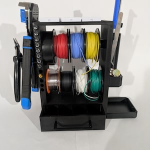 Puede incluir: Organizador de cables negro con carretes de cable rojo, azul, amarillo, negro, blanco y verde. El organizador también contiene herramientas como pelacables, alicates y un destornillador. Se incluye un cajón pequeño y una bandeja.