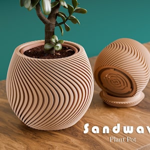 May include: A light brown, wave-patterned plant pot with a small green plant inside, next to a matching, empty pot. The text "Sandwave Plant Pot" is at the bottom of the image. The pots are on a wooden surface.