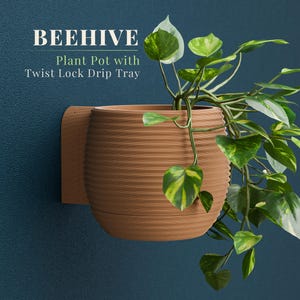 May include: A brown, ribbed plant pot with a twist-lock drip tray, mounted on a wall. The pot is filled with a green and yellow leafy plant. The text "BEEHIVE Plant Pot with Twist Lock Drip Tray" is visible.