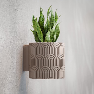 May include: A wall-mounted planter with a geometric arch pattern in a neutral taupe color. The planter holds a vibrant green snake plant. The design is modern and adds a touch of nature to interior spaces.