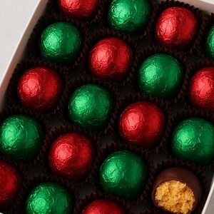 May include: A box of chocolate truffles, some wrapped in red and green foil. One truffle is cut open, revealing a peanut butter filling. The truffles are arranged in a white box with individual paper cases.