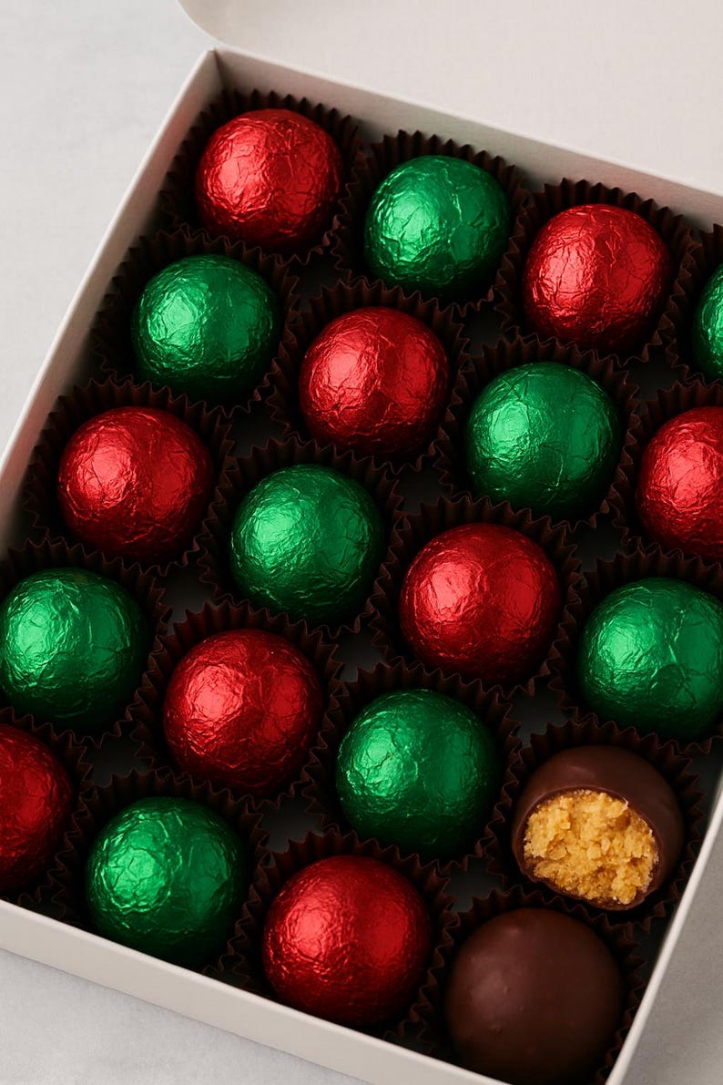 May include: A box of chocolate truffles, some wrapped in red and green foil. One truffle is cut open, revealing a peanut butter filling. The truffles are arranged in a white box with individual paper cases.