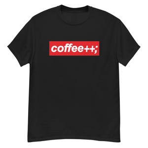 Puede incluir: Camiseta negra con un rectángulo rojo con el texto blanco "coffee++;". La camiseta tiene cuello redondo y mangas cortas. El diseño está centrado en el pecho. La tela parece suave.