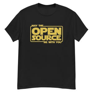 Peut inclure: T-shirt noir avec un motif rectangulaire doré portant l'inscription "OPEN SOURCE" en lettres grasses, avec "MAY THE" au-dessus et "BE WITH YOU" en dessous. Le design rappelle une célèbre franchise de science-fiction.