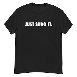 Puede incluir: Camiseta negra con el texto blanco "JUST SUDO IT.". La camiseta tiene cuello redondo y mangas cortas. El texto está centrado en el pecho.